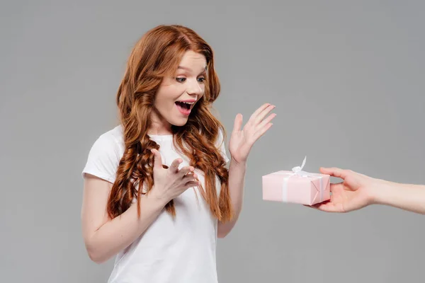 美丽的惊讶红发女孩用手指着和看着粉红色的礼品盒孤立在灰色 — 图库照片