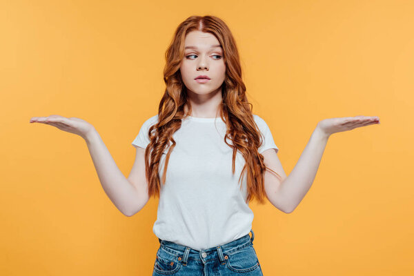 beautiful redhead girl showing shrug gesture isolated on yellow