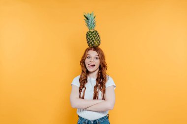 Kızıl saçlı kız kamera bakarak, dil dışarı yapışma ve sarı üzerinde izole kafası ananas ile poz