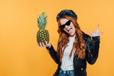 deri ceket içinde Kızıl saçlı kız ananas ile poz ve sarı üzerinde izole işareti gösteren kaya