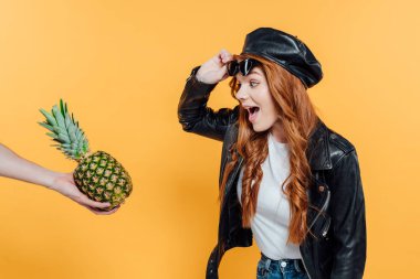 deri ceket güzel heyecanlı Redhead kız sarı üzerinde izole ananas bakıyor