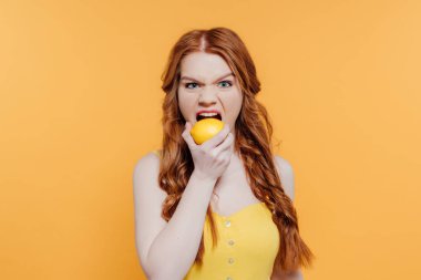 Kızıl saçlı kız kamera bakıyor, yüz ifade ve ısırma limon sarı üzerinde izole yapma