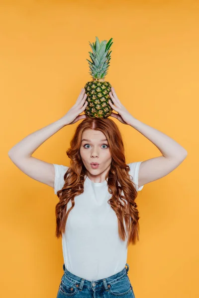 美しい赤毛の女の子は カメラを見て 顔の表情を作り 黄色に孤立した頭の上にパイナップルでポーズ — ストック写真