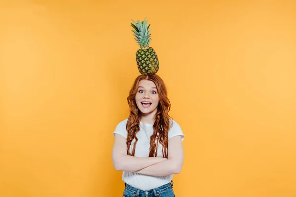 興奮した赤毛の女の子がカメラを見て 黄色に孤立した頭の上にパイナップルでポーズ — ストック写真