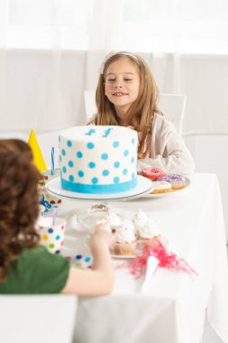 Doğum günü kutlama sırasında pasta ile parti masasında oturan sevimli çocuklar