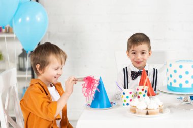 Doğum günü kutlama sırasında parti boynuz ve cupcakes ile şenlikli masada oturan sevimli preteen erkek