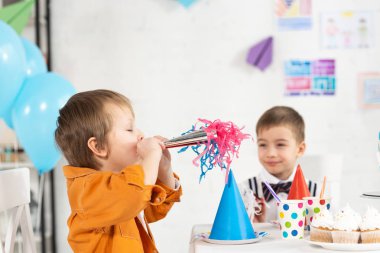 Doğum günü kutlama sırasında parti boynuz ve cupcakes ile şenlikli masada oturan sevimli preteen erkek