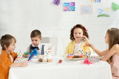 Çocuklar Doğum günü kutlama sırasında cupcakes ve parti boynuzları ile masada oturan