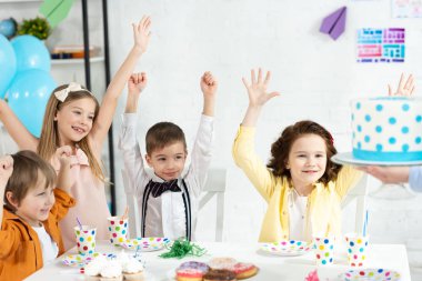 sevimli çocuklar masada oturan, tezahürat ve Doğum günü partisi sırasında pasta bekliyor