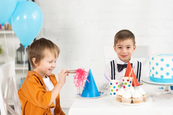 可爱的学龄前男孩坐在节日的桌子与党的号角和纸杯蛋糕在生日庆祝活动 — 图库照片