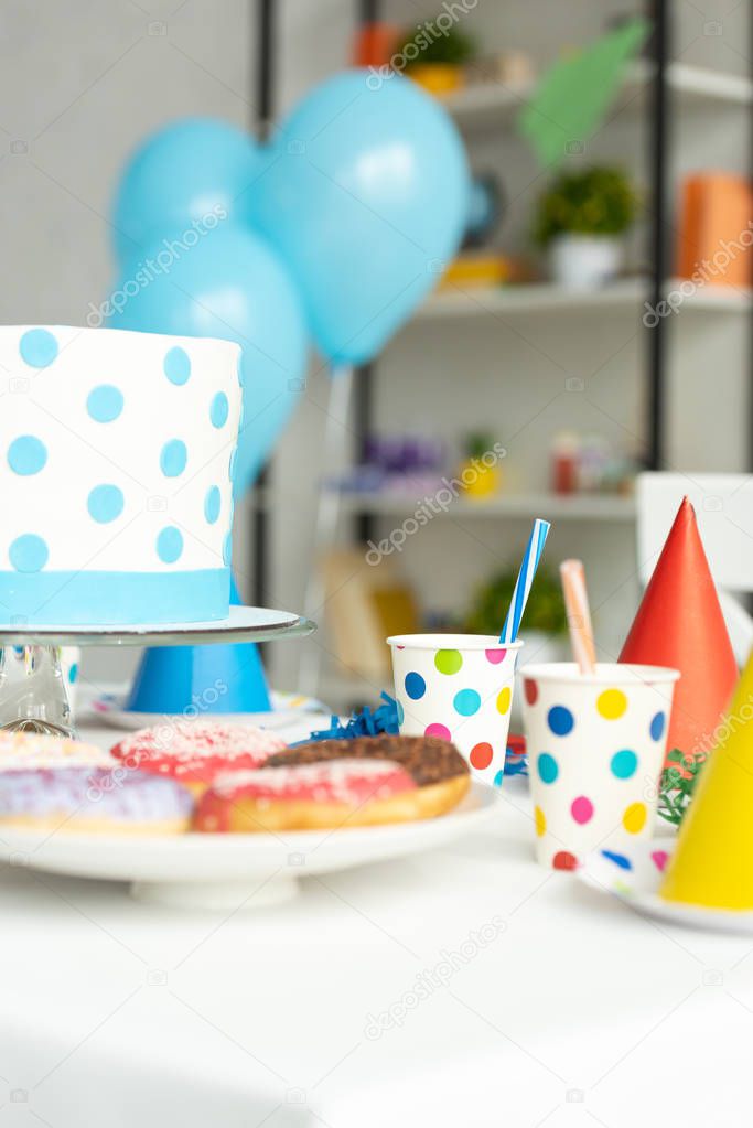 selective focus of birthday cake, donuts and party decorations on table 