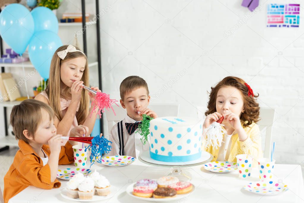 kids sitting at table with cake and blowing party horns during birthday celebration