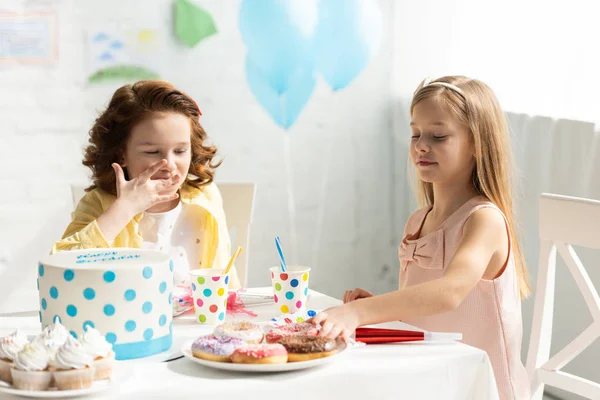 adorable kids sitting at party table with cupcakes and cake during birthday celebration