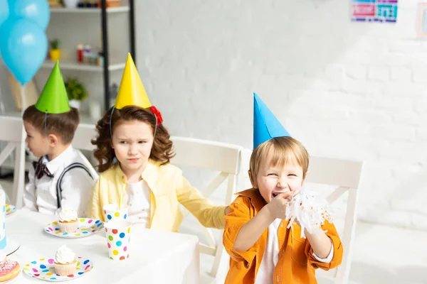 誕生日のお祝い中にお祝いのテーブルに座ってパーティーの帽子の子供たち — ストック写真