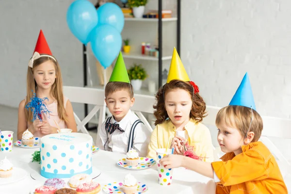 Niños Felices Sombreros Fiesta Sentados Mesa Celebrando Cumpleaños Juntos —  Fotos de Stock