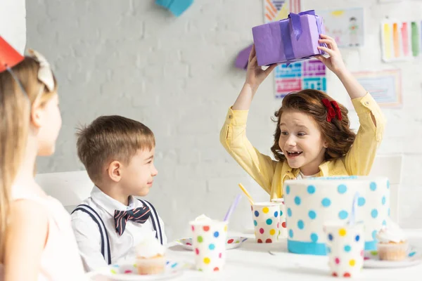 Niño Feliz Sosteniendo Presente Mientras Está Sentado Mesa Con Amigos —  Fotos de Stock