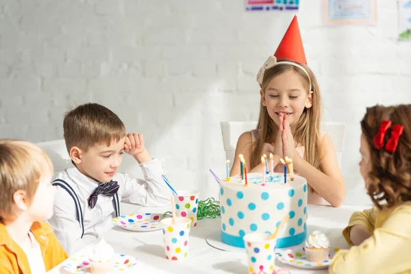 可爱的孩子做请手势和许愿 而坐在桌子上与朋友在生日聚会庆祝活动 — 图库照片