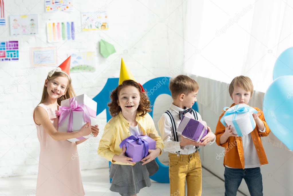 adorable smiling kids holding presents and looking at camera during birthday party at home