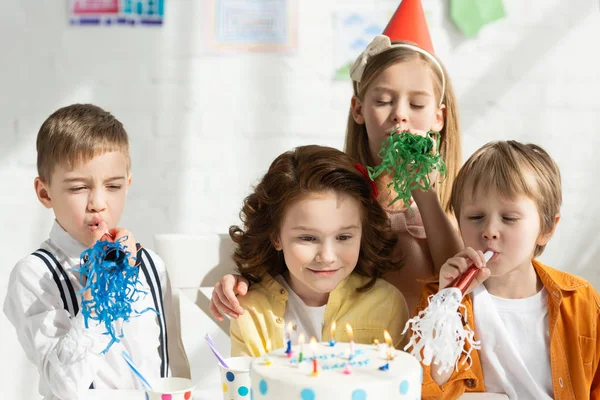 孩子们坐在桌旁吃蛋糕 在生日庆祝活动中用派对号角欢呼 — 图库照片