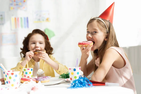 adorable kids sitting at party table and eating donuts during birthday celebration