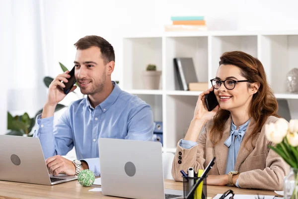 Mujer Alegre Sentada Cerca Compañero Trabajo Hablando Teléfono Inteligente Oficina — Foto de Stock