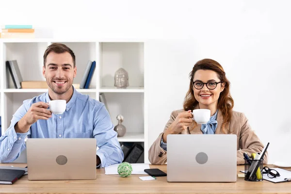 Alegre Empresaria Gafas Sosteniendo Taza Cerca Compañero Trabajo Oficina —  Fotos de Stock