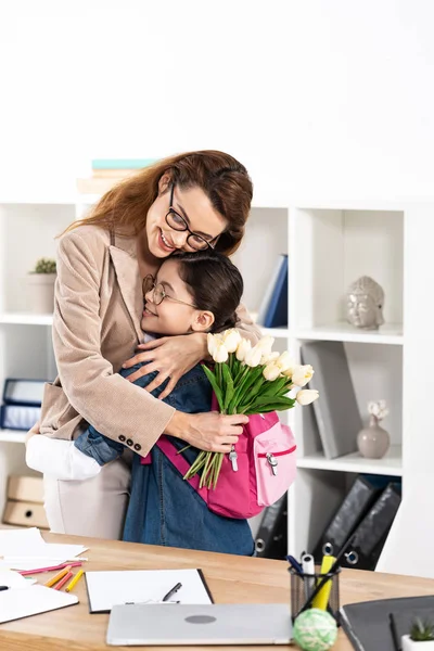 Mãe Feliz Abraçando Filha Bonito Segurando Flores Escritório — Fotografia de Stock