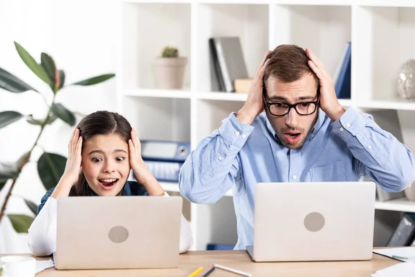 震惊的父亲和女儿看着笔记本电脑 并在办公室保持头 — 图库照片