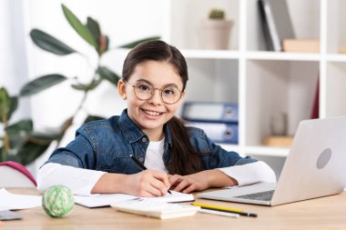 ofiste dizüstü bilgisayar yakınında kamera bakarak mutlu sevimli çocuk 