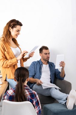 evde dijital tablet kullanarak anne ve baba yakınında oturan çocuğun arka görünümü 