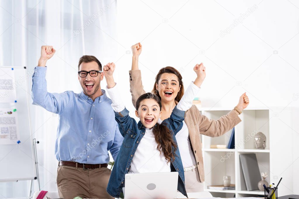 cheerful family celebrating triumph near laptop in office 