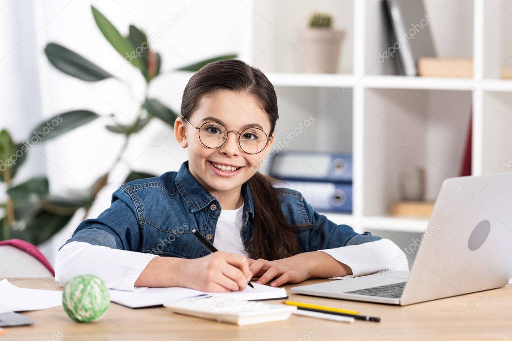 happy cute kid looking at camera near laptop in office 