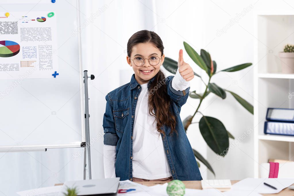 cheerful kid showing thumb up near white board with charts and graphs 