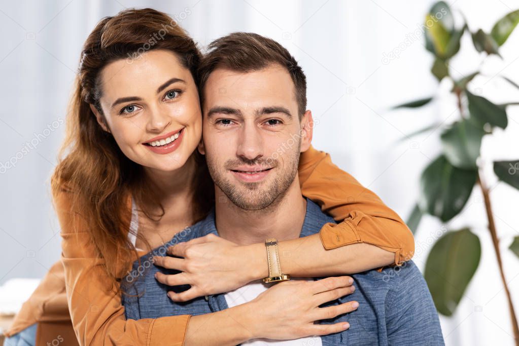 cheerful woman hugging happy man and smiling at home 