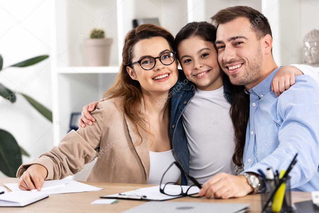 cheerful and cute kid hugging happy parents in office 