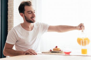 gülümseyen sakallı adam cam portakal suyu dökerek