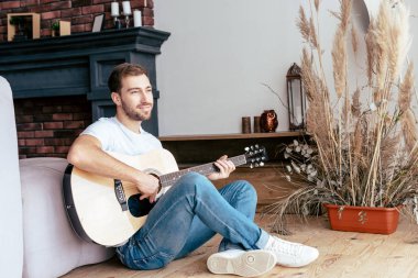 oturma odasında akustik gitar çalan gülümseyen sakallı adam