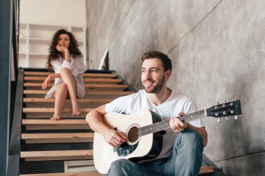 gülümseyen sakallı adam merdivenlerde oturan ve kız arkadaşı akustik gitar çalmak