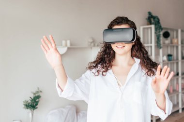 vr kulaklık içinde gülümseyen kız yatak odasında el sallayarak