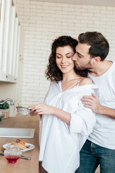 man kissing girlfriend while she preparing breakfast in kitchen