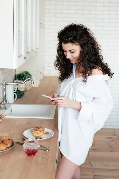 Gadis Cantik Tersenyum Dengan Kemeja Putih Menggunakan Smartphone Dapur — Stok Foto