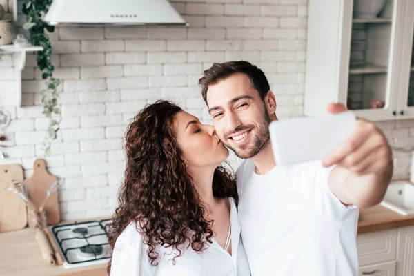 Menina Encaracolado Beijando Namorado Enquanto Ele Tomando Selfie Cozinha — Fotografia de Stock