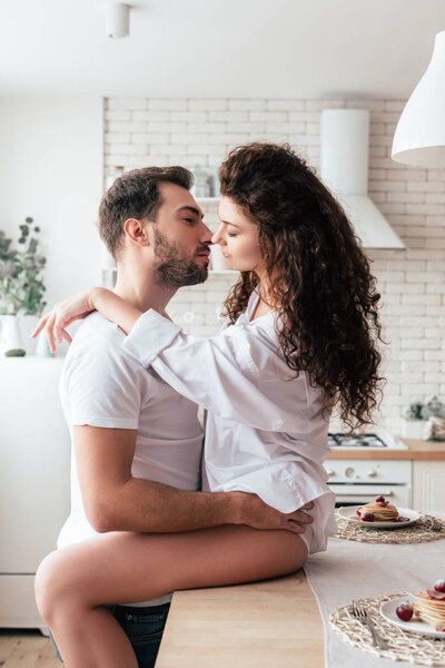 sexy girl sitting on table and embracing with boyfriend in kitchen