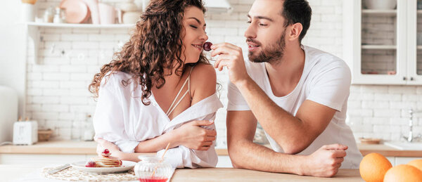 panoramic shot of bearded man feeding girlfriend with berry