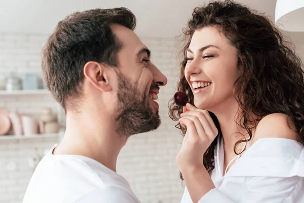 Laughing Curly Woman Feeding Boyfriend Berry Kitchen — Stock Photo, Image