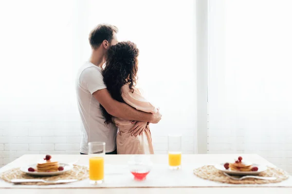 夫妇拥抱和望向附近服务表与早餐 — 图库照片