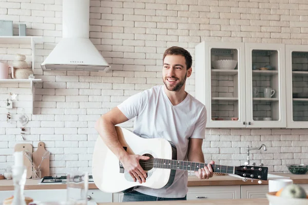 Sorrindo Homem Tocando Guitarra Acústica Olhando Para Longe Cozinha — Fotografia de Stock