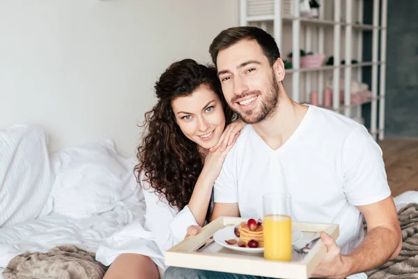 微笑的夫妇坐在床上 拿着托盘与早餐 — 图库照片