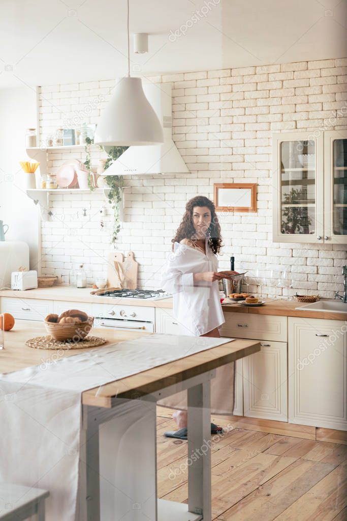 Pretty woman in white shirt looking away while preparing breakfast in kitchen