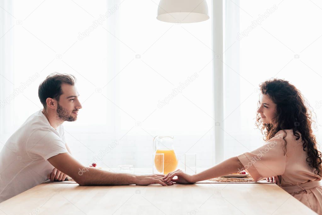 couple touching hands and looking at each other at table during breakfast